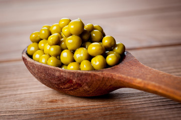Canned green peas in a wooden spoon lying on a wooden surface of the table.