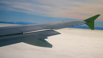 Airplane. A beautiful wing of an airplane flying high in the sky, above clouds, small towns, forests and fields. Closeup. Travel, tourism and vacation concept.For design. 