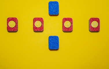Colored dishwasher tablets on a yellow background. Minimalist design composition