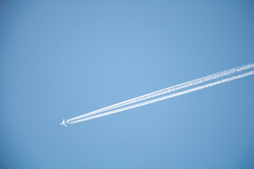 A plane is flying in the blue sky at high altitude. And leaves a white line behind