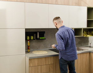 A bearded man stands with his back to the camera next to a work surface in a modern kitchen