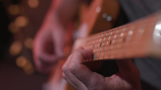Male guitar player practices scales on electric guitar in music studio, closeup
