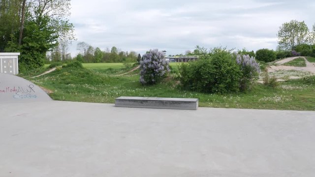 Medium wide shot of a small curb on an skatepark in Erbach, Germany. Parallax shot with deep depth of field. Dirt track for mountain biking in the background.