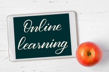 Online learning - handwritten inscription on a tablet. The concept of distance training for children. Tablet and Apple on a white wooden background.