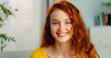Portrait of beautiful cheerful redhead girl smiling looking at camera sitting on sofa at home.