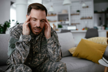 Depressed soldier sitting on sofa in living room. Young marine having PTSD.
