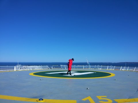 A child in a red coat with a backpack walks on the upper deck of a ship that sails on the sea