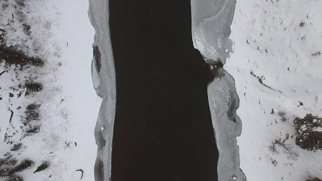 Aerial view of river surrounded by ice sheet and snow during winter, drone ascending over water by vehicle on road - Jackson, Wyoming