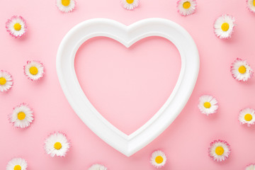 White frame of heart shape and colorful daisies on light pink table background. Pastel color. Love...