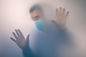 Man in medical mask behind frosted glass. Concept on the topic of quarantine in a hospital....