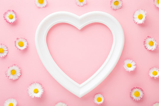 White frame of heart shape and colorful daisies on light pink table background. Pastel color. Love and happiness concept. Empty place for cute, emotional, sentimental text, quote or sayings. Top view.