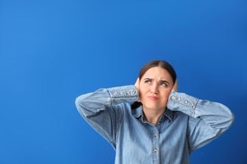 Young woman suffering from loud noise on color background