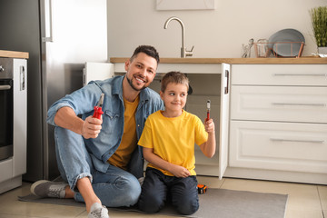Little son helping his father to repair sink in kitchen