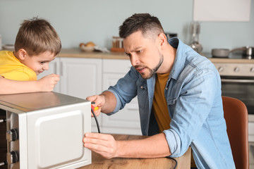 Obraz premium Little son helping his father to repair microwave oven in kitchen