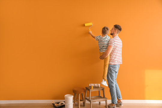 Little son helping his father to paint wall at home