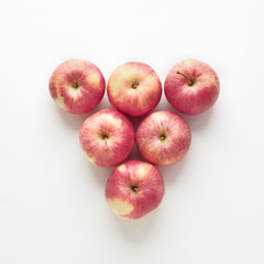 Fresh red apples laid out in the shape of a triangle on a white background. Fruit composition, pattern, vitamin food poster. Square, top view, flat lay with copy space.