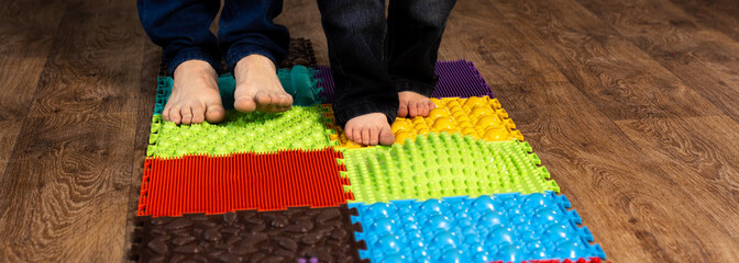 adult and children's feet on orthopedic rug close-up. panoramic photo. prevention of flat feet at home. foot massage with different types of surfaces.