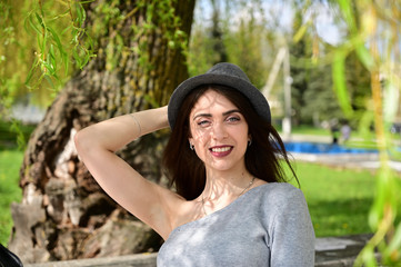 Close-up portrait of a cute young caucasian brunette girl in a gray dress and black hat in various poses. Model posing in spring park outdoors with a smile.