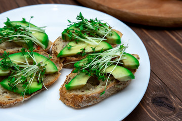 sandwiches with avocado and cressalate microgreens on a white plate on a window background. healthy diet. feed option. vegetarianism.
