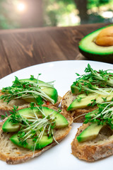 sandwiches with avocado and cressalate microgreens on a white plate on a window background. healthy diet. feed option. vegetarianism.