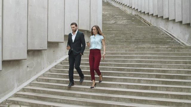 Confident colleagues going down stairs. Man and woman talking on street