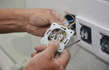 An electrician is installing, adding new electrical socket, connecting power socket outlet, wires while home renovating.