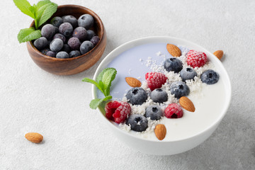 Healthy Breakfast smoothie in a bowl with coconut milk, blue matcha, raspberries, blueberries, almonds and fresh mint.