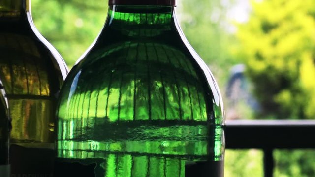 A selection of green glass bottles, sideways movement with railings and a blurred lush garden background