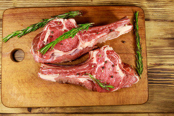 Raw fresh beef rib eye steaks on bone with spices and rosemary on wooden table. Top view