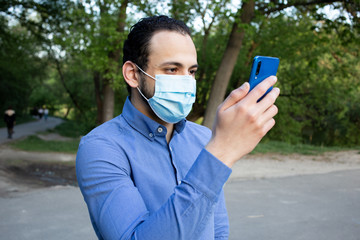 A portrait of the young man from Middle Eastern in a protective mask in the park. A man looks at...