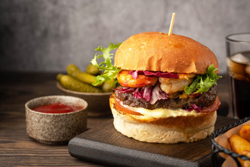 Shrimp and beef burger, drink glass, fried potato wedges, cucumber and sause. Close-up, light background.