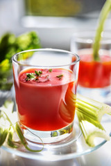 Two glasses of tomato juice with parsley and celery decorations, stand near the window, morning sunlight shines, shallow depth of field, selective focus. Natural drinks concept.