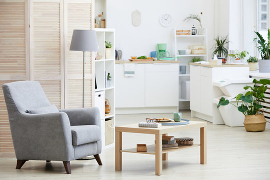 Image of armchair and wooden table in the living room with modern kitchen in the background