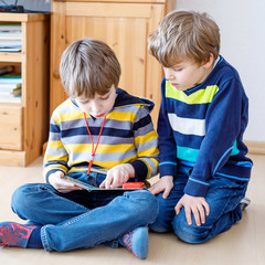 Two little kid boys reading a book at home. Older schoolboy reading for his brother, preschool sibling a fairytale or story. Family, children, education and leisure..