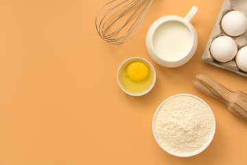 Baking Ingredient- flour, egg, milk, rolling pin, whisk on a pastel yellow background. Top view, flat lay, copy space.