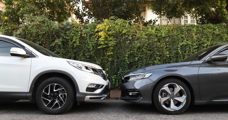 Closeup of front side of white and grey cars  parking in the opposite direction with natural background. 