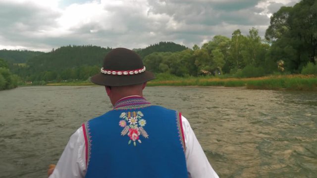 Clothed in folk costume mountain raftsman steering the raft. View from behind the person.