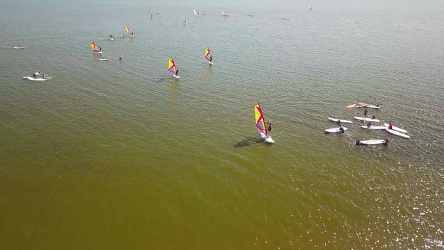 Epic drone shot of entry-level windsurfer. Camera pulls away revealing vastness of lake and multitude of other windsurfers,