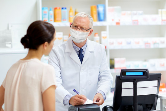 medicine, healthcare and people concept - senior apothecary wearing face protective medical mask for protection from virus disease writing prescription for female customer at pharmacy