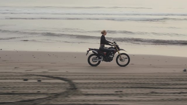 Woman traveler riding mountain bike along empty sand beach