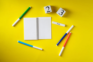 Date on the calendar July 23, notebook, felt-tip pens, on a yellow background