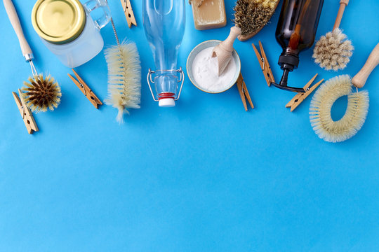 natural cleaning stuff, sustainability and eco living concept - washing soda, bottle of vinegar, clothespins with laundry and liquid soap and brushes on blue background