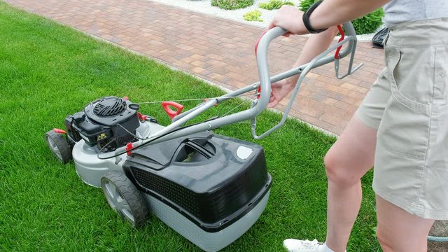 A woman starts a lawn mower. Mowing green grass. Side and top view.