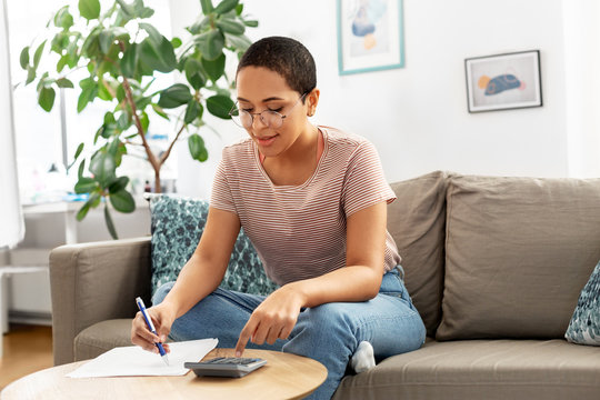 accounting, taxes and finances concept - young african american woman in glasses with papers and calculator at home