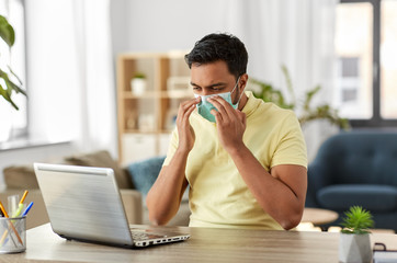 quarantine, remote job and pandemic concept - happy indian man wearing face protective medical mask for protection from virus disease with laptop computer working at home office