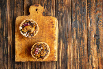 Tarts with mushrooms, caramelized red onion and cheese over on old wooden rustic background.