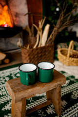 two green cups stand on a stool against the background of the hearth in the cottage. Winter theme