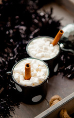 two black cups with hot cocoa and marshmallows with cinnamon sticks. Drinks for winter
