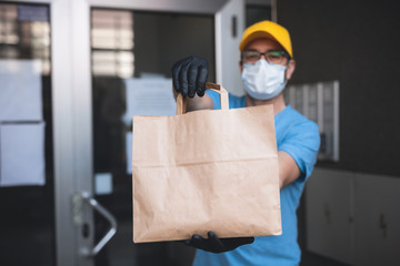Fototapeta na wymiar Delivery guy with protective mask and gloves holding box / bag with groceries in front of a building.