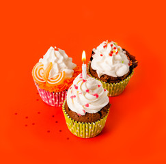 three cupcakes with a candle cream on an orange background
